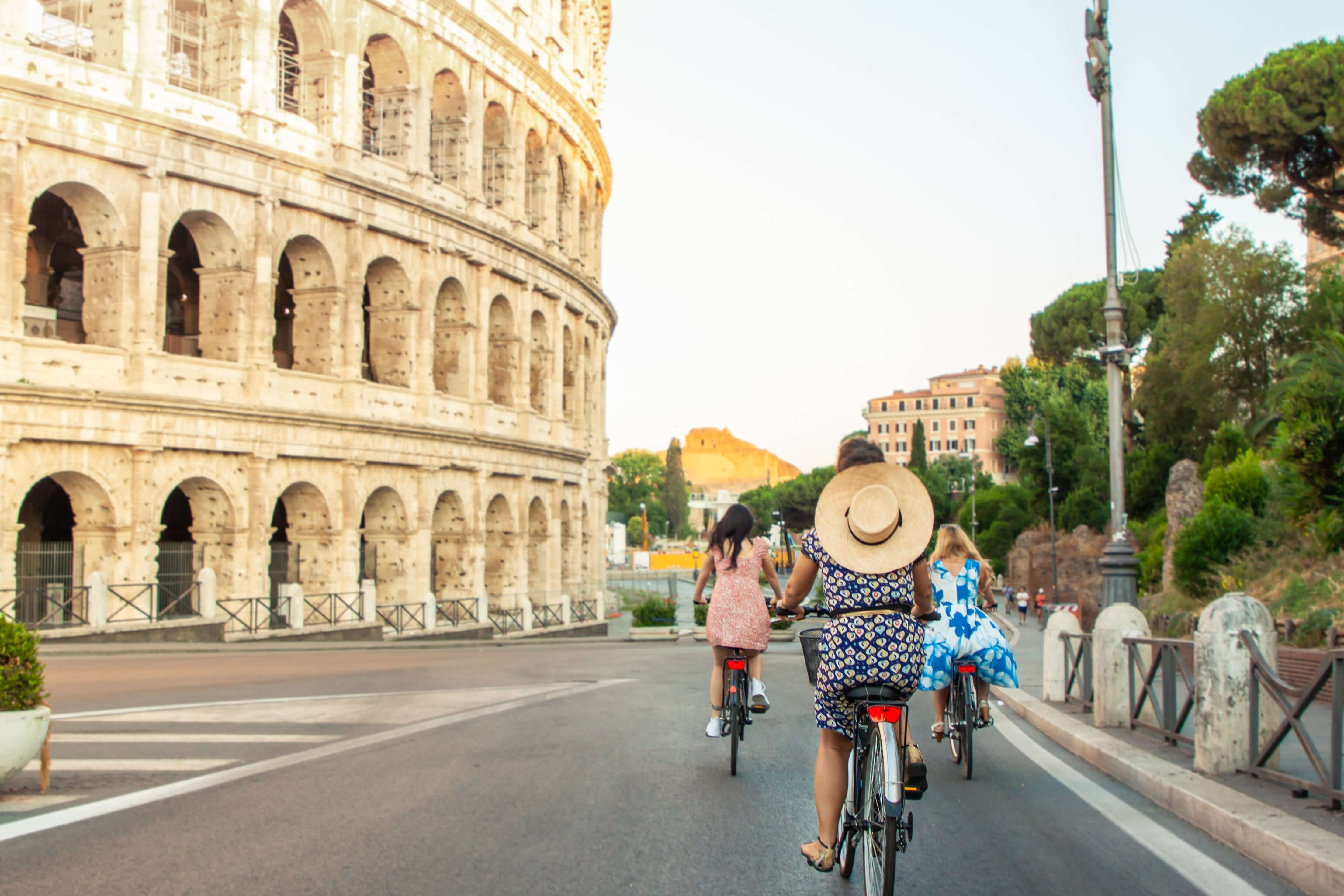 Three happy young women friends tourists with bikes at Colosseum in Rome, Italy at sunrise.